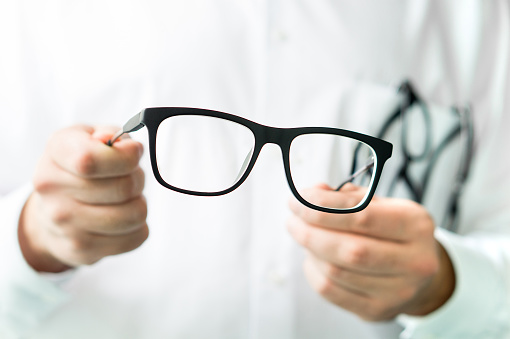 Optician holding glasses. Eye doctor showing new lenses. Professional optometrist in white coat.